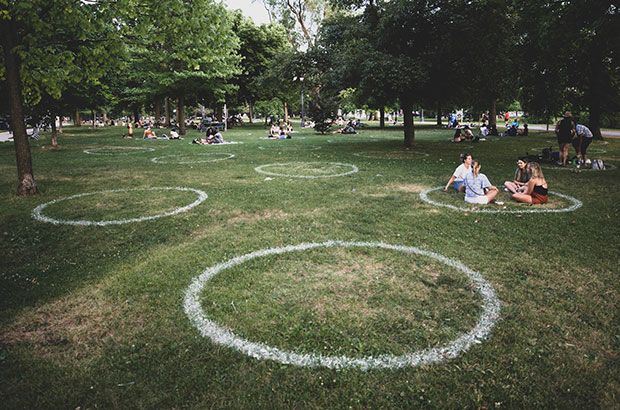 Groups of people in a park are clustered inside marked circles to demonstrate the changes in public spaces during COVID19