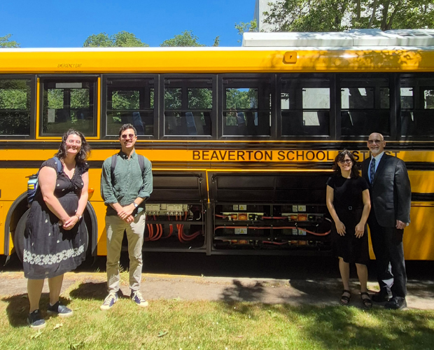 Climate advocates and school district employees standing in front of an electric school bus with the giant electric batteries exposed.
