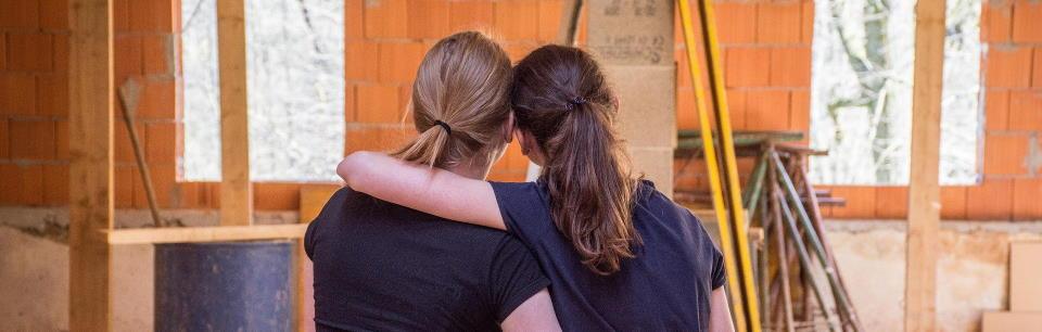 Photo of two women hugging in a home under construction