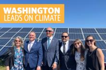 text 'washington leads on climate' above solar panel array with group of people including gov inslee in front smiling