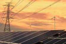 solar panels and wind turbines and transmission lines against a sunset backdrop